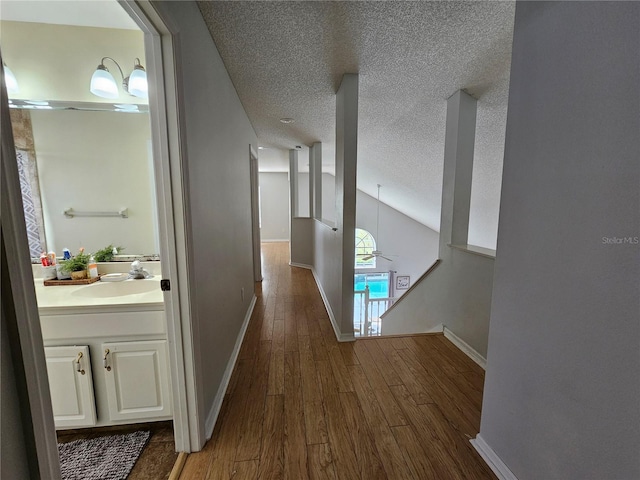 corridor with a textured ceiling, dark hardwood / wood-style flooring, lofted ceiling, and sink