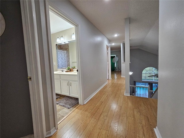 hallway featuring lofted ceiling, sink, light hardwood / wood-style floors, and a textured ceiling