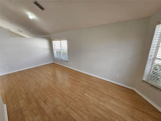 empty room featuring a textured ceiling, light wood-type flooring, and vaulted ceiling