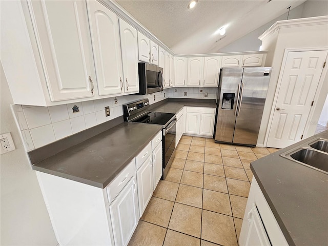 kitchen featuring vaulted ceiling, light tile patterned flooring, tasteful backsplash, white cabinets, and stainless steel appliances