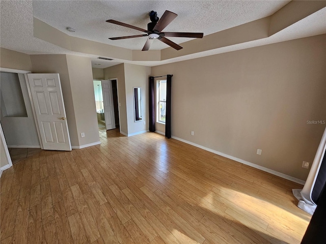 unfurnished room with ceiling fan, a textured ceiling, light hardwood / wood-style floors, and a tray ceiling