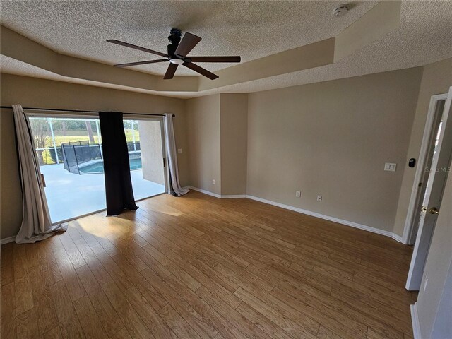 spare room with ceiling fan, a tray ceiling, a textured ceiling, and hardwood / wood-style flooring