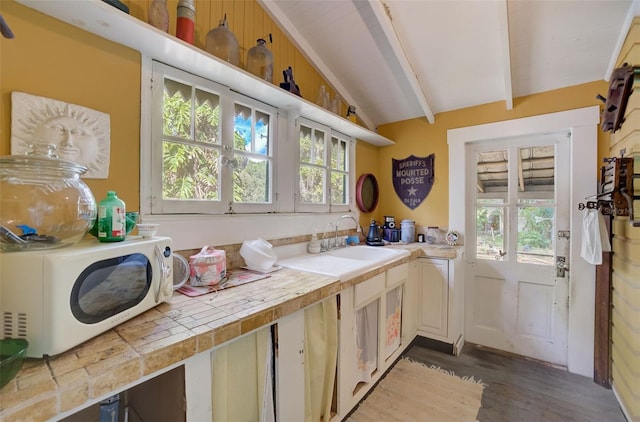 kitchen with tile countertops, a healthy amount of sunlight, vaulted ceiling with beams, and wood-type flooring