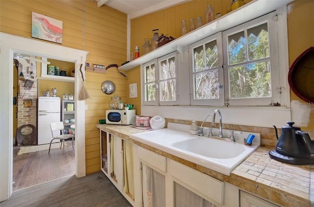 interior space featuring dark hardwood / wood-style flooring, brick wall, sink, wood walls, and refrigerator