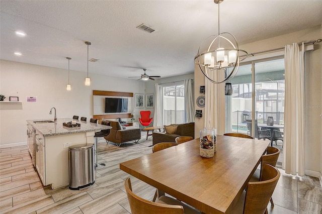 dining space featuring a textured ceiling, ceiling fan with notable chandelier, and sink