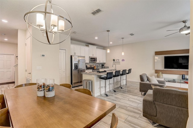 dining space featuring light hardwood / wood-style floors, ceiling fan with notable chandelier, and sink