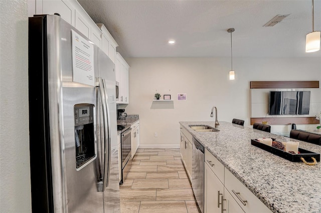 kitchen with light stone countertops, hanging light fixtures, white cabinetry, sink, and stainless steel appliances