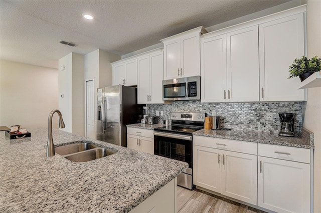 kitchen with stainless steel appliances, tasteful backsplash, sink, white cabinets, and light stone counters