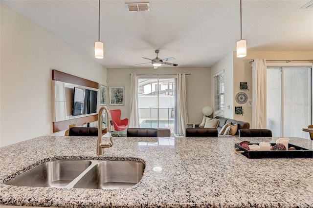 kitchen featuring decorative light fixtures, ceiling fan, sink, and light stone countertops