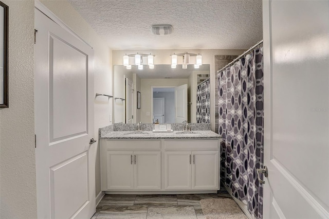 bathroom featuring a textured ceiling, dual bowl vanity, and tile flooring