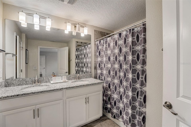 bathroom with a textured ceiling, dual sinks, and vanity with extensive cabinet space