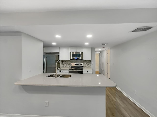 kitchen with stainless steel appliances, tasteful backsplash, light hardwood / wood-style flooring, white cabinets, and sink