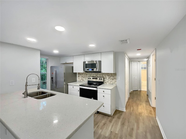 kitchen with light stone countertops, white cabinetry, light hardwood / wood-style floors, sink, and stainless steel appliances