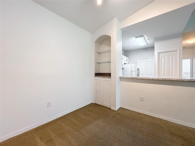 unfurnished room with built in features, dark colored carpet, and lofted ceiling