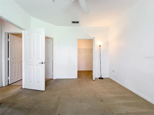 unfurnished bedroom with a closet, dark carpet, a spacious closet, and ceiling fan