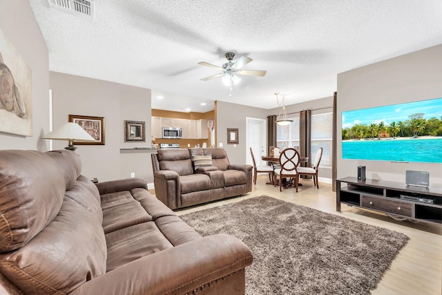 living room featuring ceiling fan, light hardwood / wood-style floors, and a textured ceiling