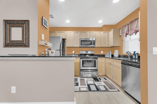 kitchen featuring light brown cabinets, dark stone counters, light hardwood / wood-style flooring, and stainless steel appliances