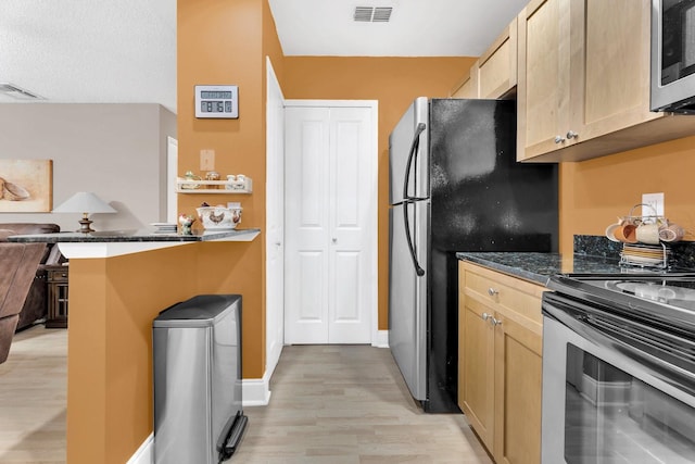 kitchen with kitchen peninsula, appliances with stainless steel finishes, light brown cabinets, light hardwood / wood-style flooring, and dark stone countertops