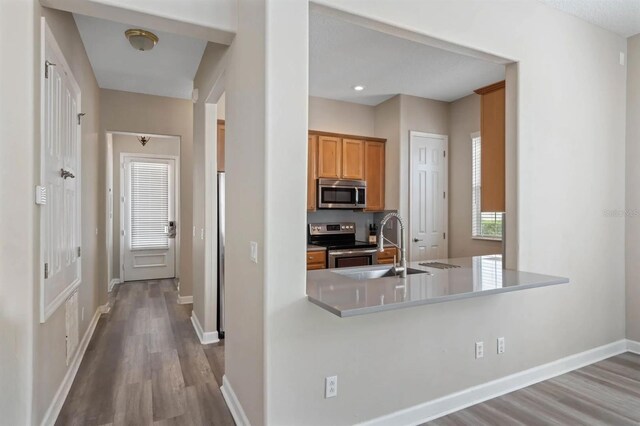 kitchen with appliances with stainless steel finishes, light hardwood / wood-style flooring, sink, and kitchen peninsula