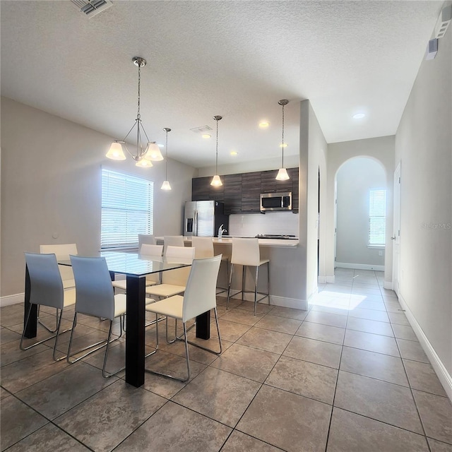 tiled dining area featuring a chandelier, plenty of natural light, and a textured ceiling