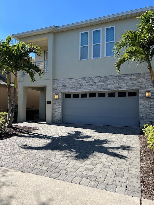 view of front of home featuring stone siding, decorative driveway, and stucco siding