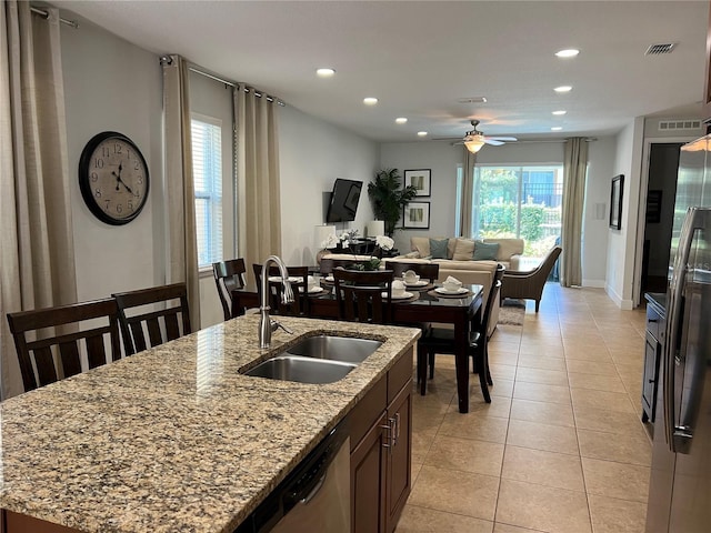 kitchen with visible vents, light stone countertops, a kitchen island with sink, a sink, and light tile patterned flooring