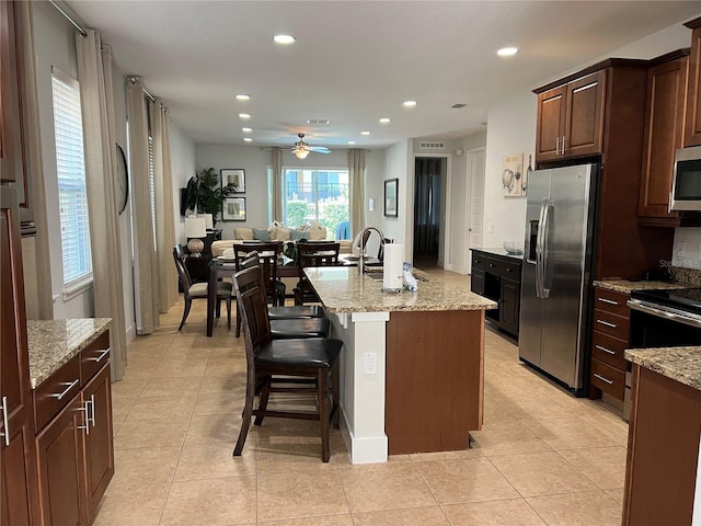 kitchen with light stone counters, stainless steel appliances, open floor plan, a kitchen bar, and a center island with sink