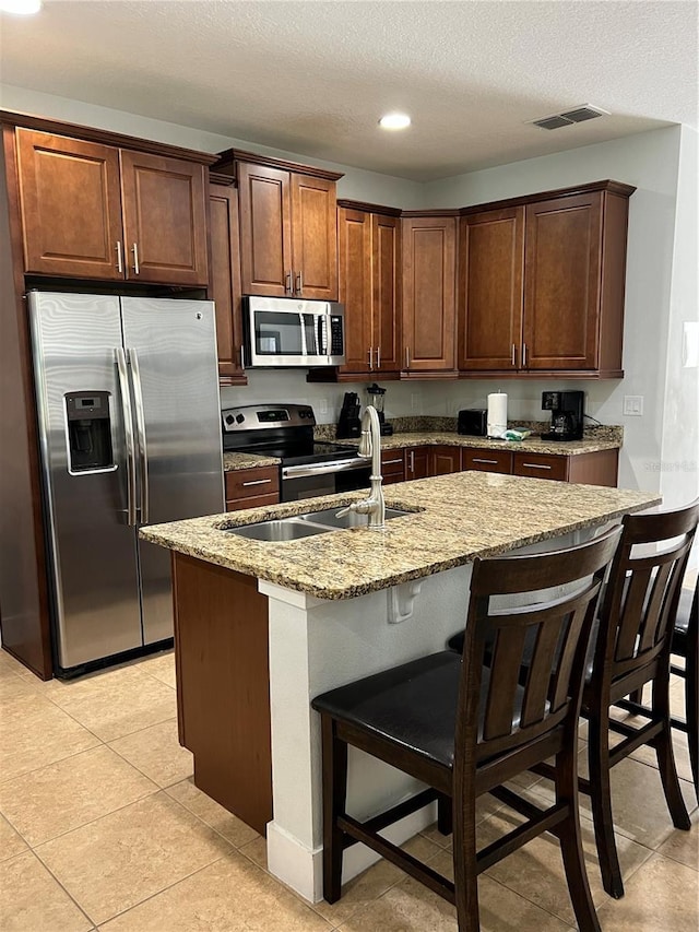 kitchen featuring light stone counters, a sink, a kitchen breakfast bar, appliances with stainless steel finishes, and a center island with sink