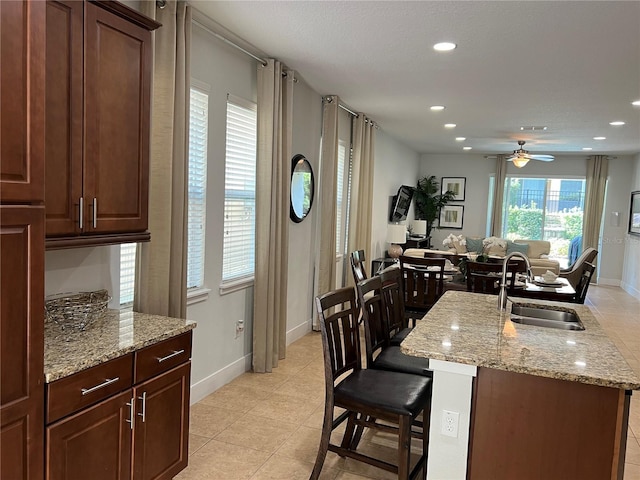 kitchen with light stone counters, recessed lighting, a breakfast bar, a sink, and an island with sink