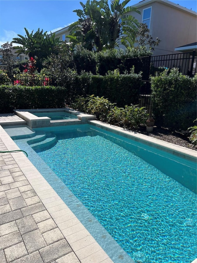 view of swimming pool featuring a pool with connected hot tub and fence