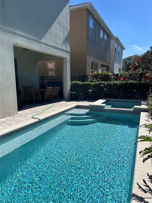 view of pool featuring a patio, fence, and a pool with connected hot tub