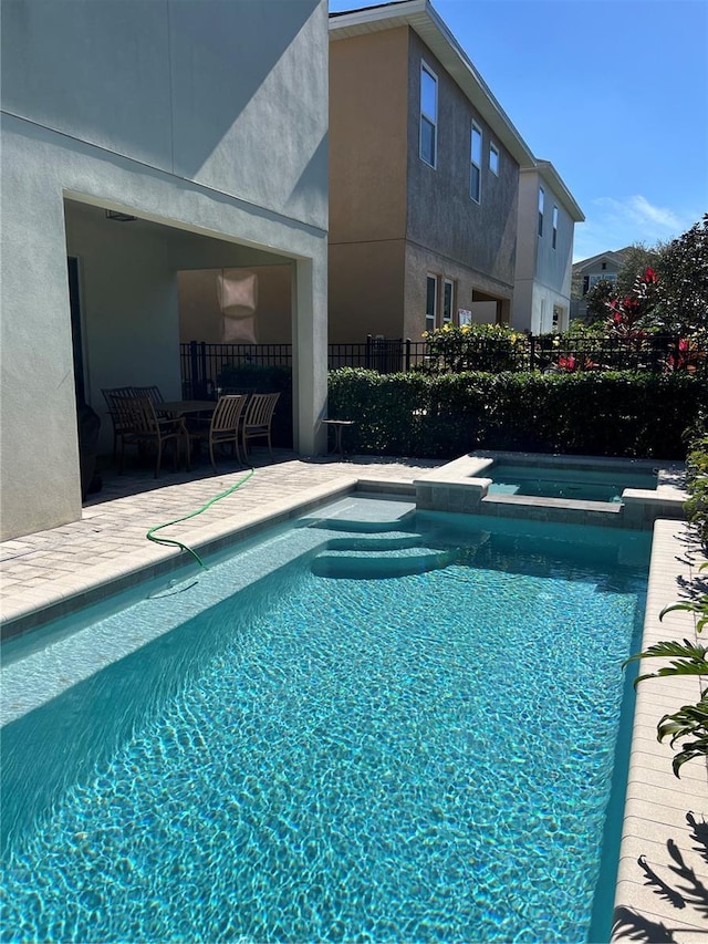 view of pool featuring a patio area, a pool with connected hot tub, and fence