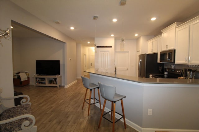 kitchen with white cabinetry, hanging light fixtures, dark wood-type flooring, a breakfast bar area, and appliances with stainless steel finishes