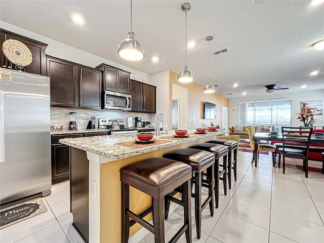 kitchen featuring pendant lighting, a kitchen breakfast bar, ceiling fan, appliances with stainless steel finishes, and a kitchen island with sink