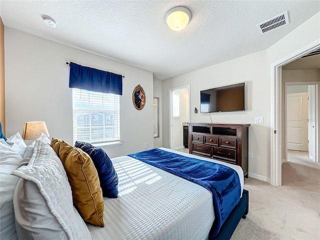 bedroom featuring light carpet, a textured ceiling, and ensuite bathroom