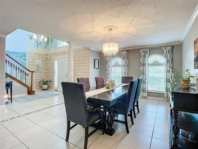 tiled dining space with brick wall, crown molding, decorative columns, an inviting chandelier, and a textured ceiling