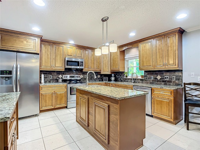 kitchen featuring an island with sink, appliances with stainless steel finishes, backsplash, hanging light fixtures, and light stone counters