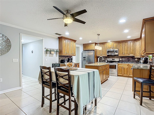 kitchen with ceiling fan, light tile flooring, stainless steel appliances, a center island with sink, and pendant lighting