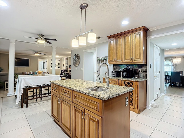 kitchen featuring decorative light fixtures, backsplash, ceiling fan with notable chandelier, sink, and a center island with sink