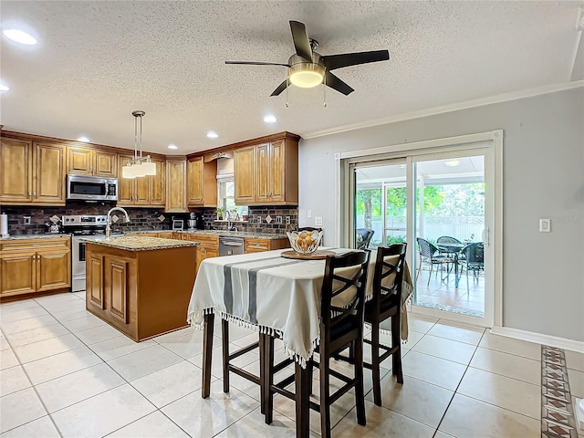 kitchen with pendant lighting, ceiling fan, a center island with sink, appliances with stainless steel finishes, and light stone counters