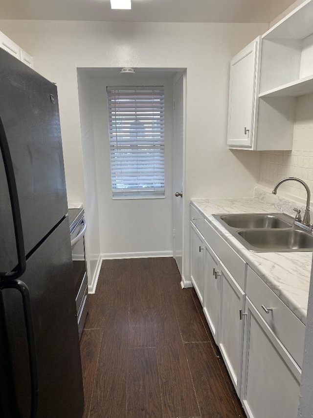 kitchen with black refrigerator, backsplash, dark hardwood / wood-style floors, sink, and white cabinets