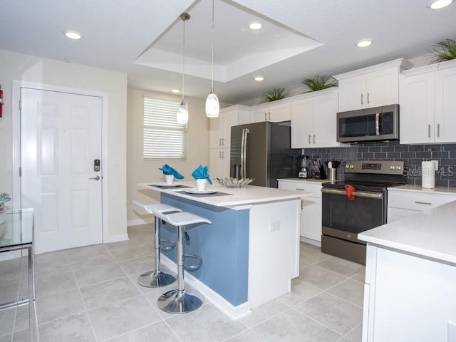 kitchen with pendant lighting, a tray ceiling, white cabinets, appliances with stainless steel finishes, and a center island