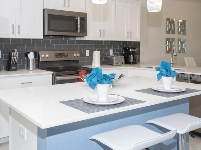 kitchen with decorative backsplash, stainless steel appliances, white cabinetry, and a breakfast bar area