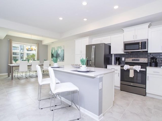 kitchen with appliances with stainless steel finishes, tasteful backsplash, an inviting chandelier, and white cabinets