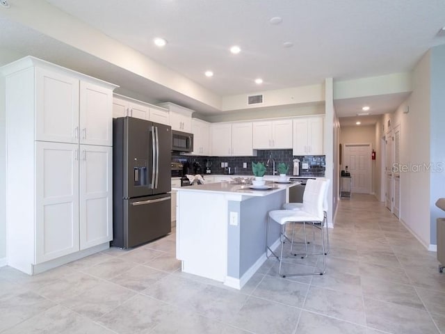 kitchen with appliances with stainless steel finishes, a kitchen island, white cabinets, and decorative backsplash