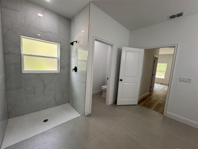 bathroom featuring tiled shower, tile flooring, toilet, and a textured ceiling