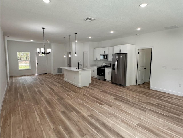 kitchen with stainless steel appliances, light wood-type flooring, hanging light fixtures, a kitchen island with sink, and white cabinetry