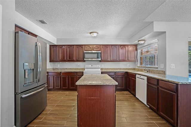 kitchen with light stone countertops, stainless steel appliances, sink, a kitchen island, and a textured ceiling