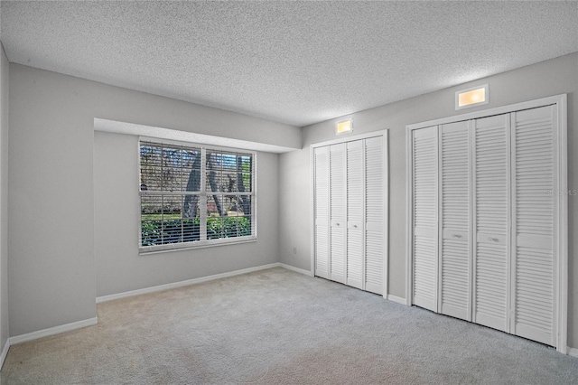 unfurnished bedroom featuring a textured ceiling, two closets, and light carpet