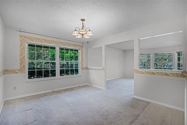 carpeted spare room featuring a textured ceiling and an inviting chandelier